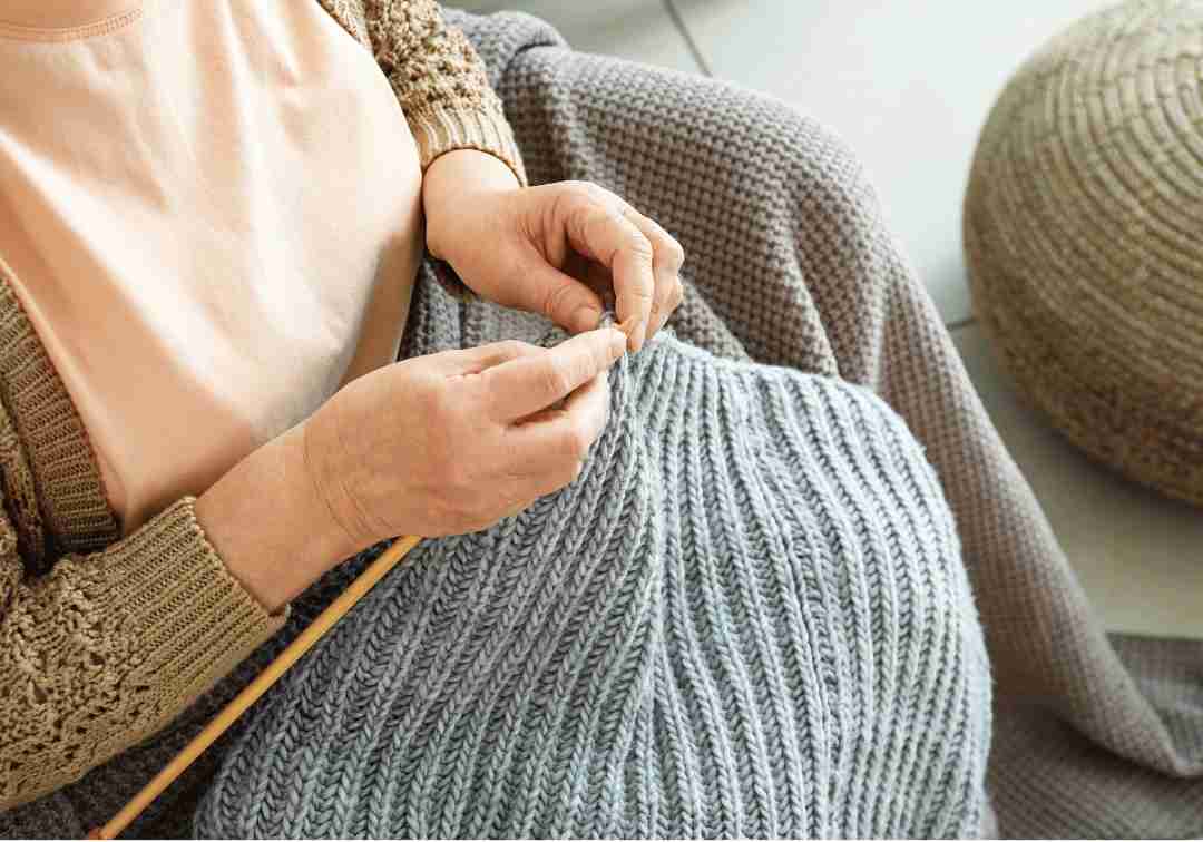 Close-up of a senior's hands knitting with gray yarn.
