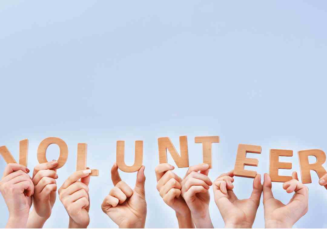 Hands holding up individual letters spelling out the word 'volunteer'.
